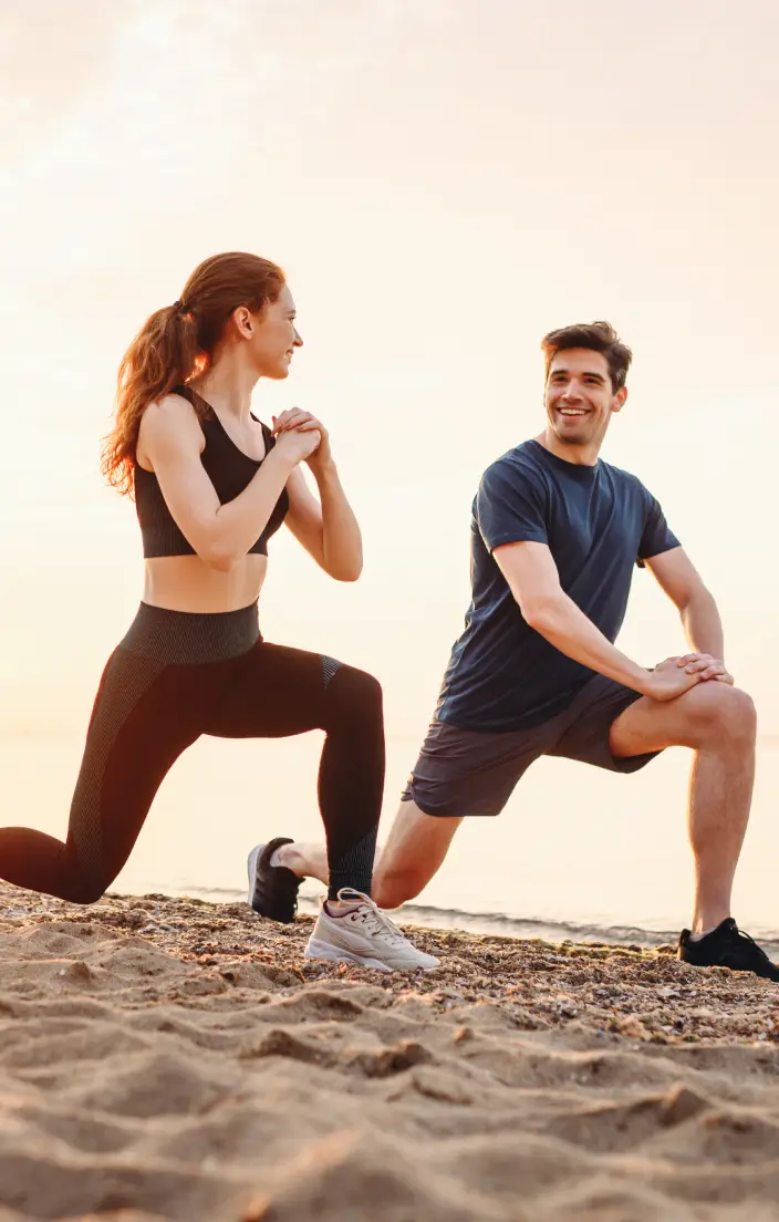 Two people stretching on a beach, smiling.