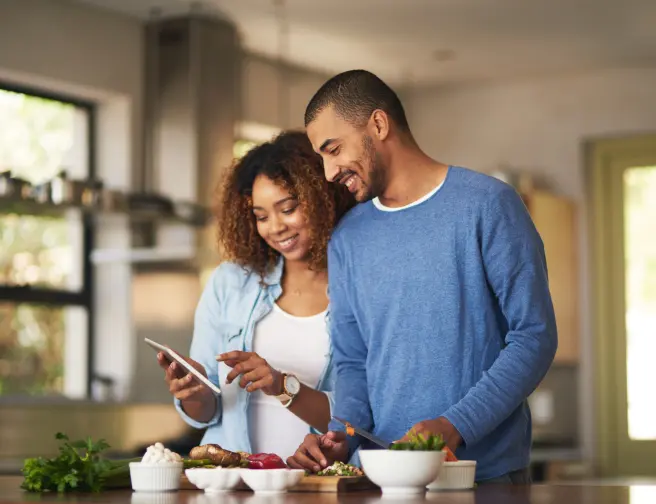 Man and a woman smiling, looking at a tablet.